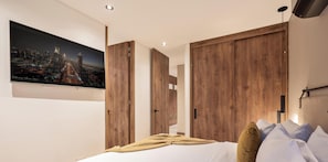 A modern bedroom with a bed, wooden wardrobe, and a cityscape TV.