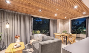 A modern living room with a sofa, a dining table, and a balcony with a view of the city at night.