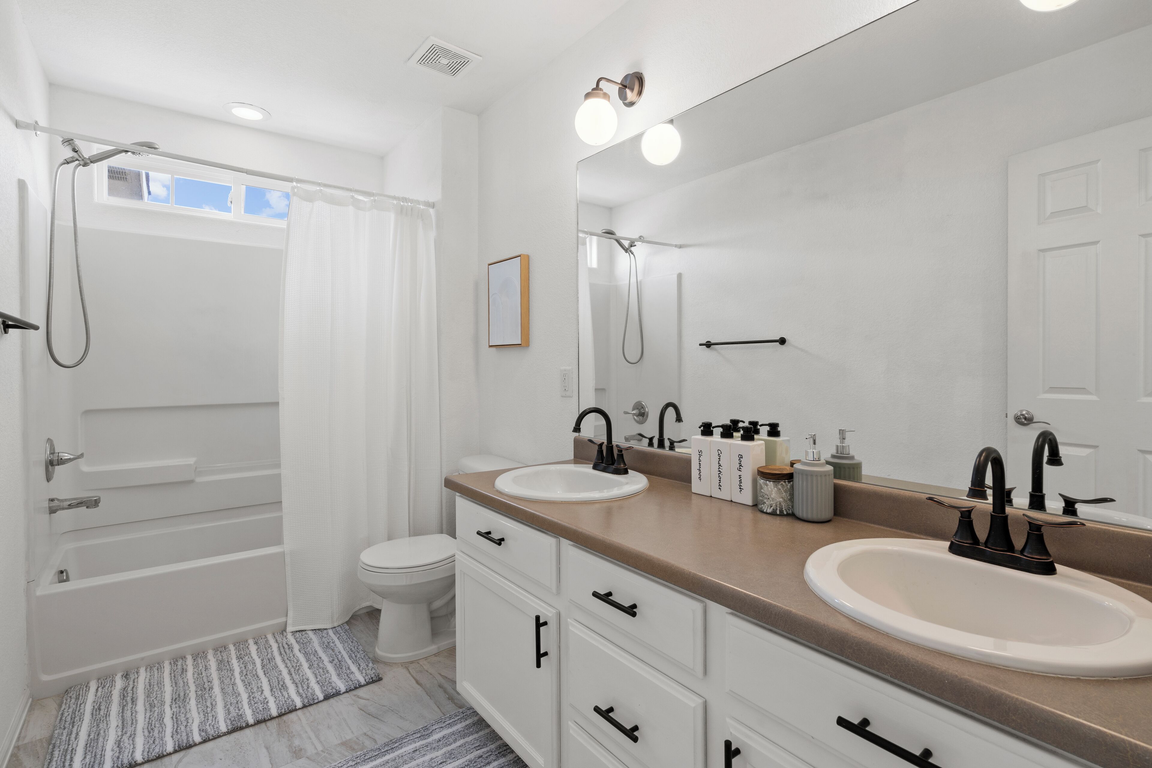 Een moderne badkamer met twee wastafels, een douche en een grote spiegel.