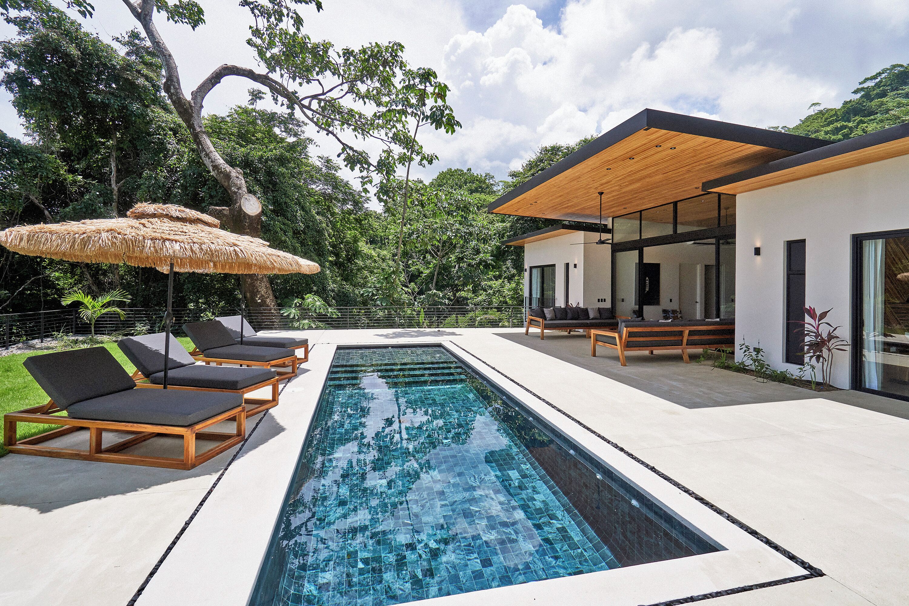 A modern outdoor pool area with lounge chairs, a wooden pergola, and a glass-enclosed patio.