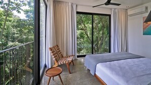 A bedroom with a bed, a chair, a balcony with a railing, and a view of trees. - Villa Alba (Cóbano)