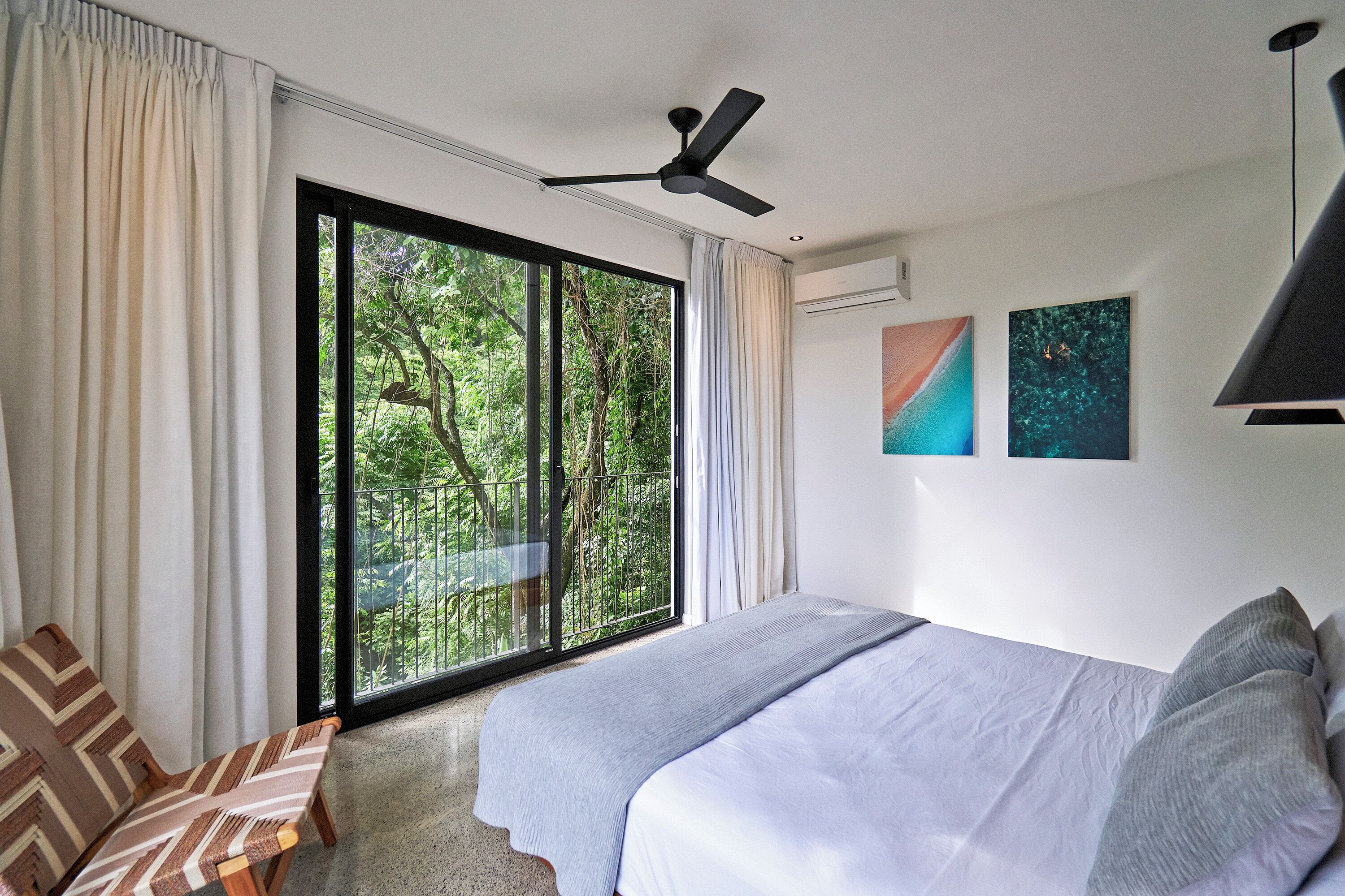 A bedroom with a bed, a ceiling fan, a window with curtains, and a view of greenery outside.