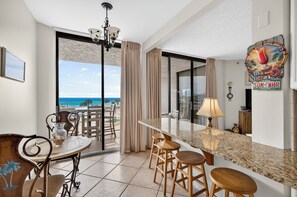 A modern kitchen with a large island, a dining area with a view of the ocean, and a bar area with stools. - Free Beach SRVC! Free Beach Bonfires M/F nts! Sports Deck w/Pickleball (Miramar Beach)
