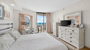 Een slaapkamer met een groot bed, een dressoir, een televisie en een balkon met uitzicht op zee.