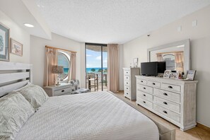 Een slaapkamer met een groot bed, een dressoir, een televisie en een balkon met uitzicht op zee.