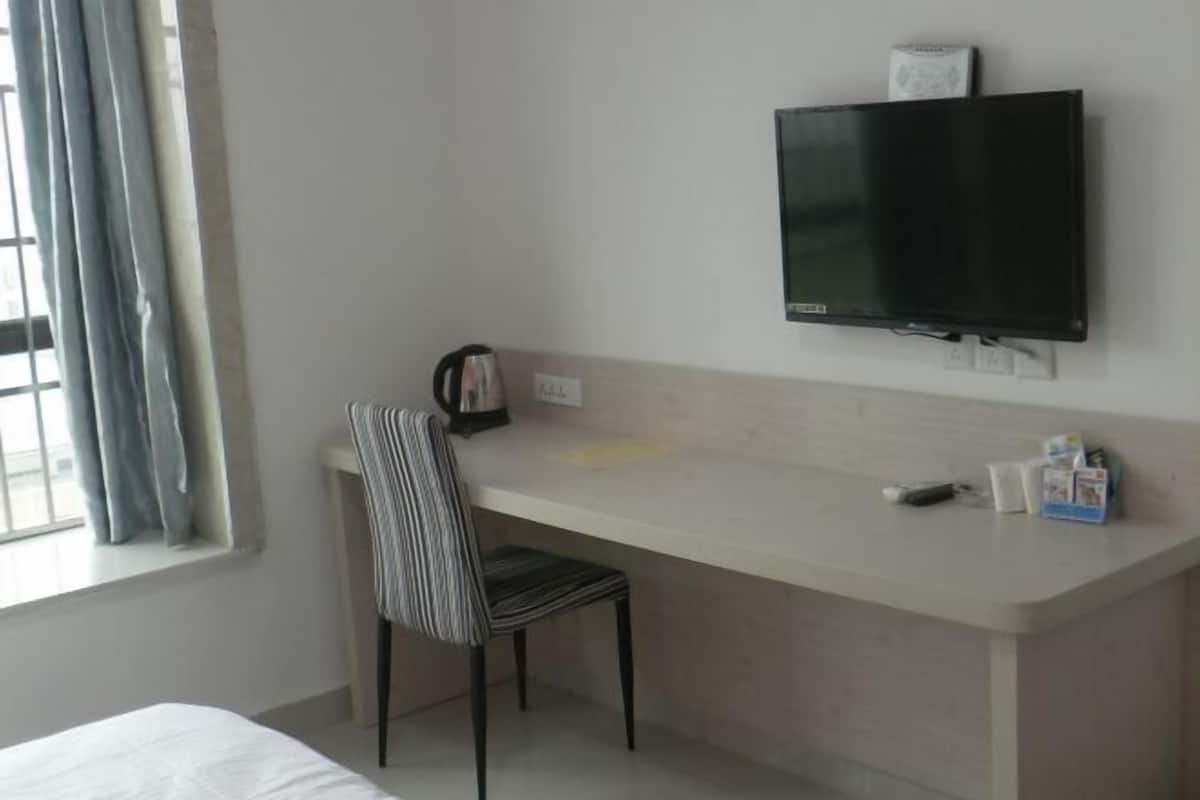 A hotel room with a bed, a desk with a chair, a television mounted on the wall, and a window with curtains.