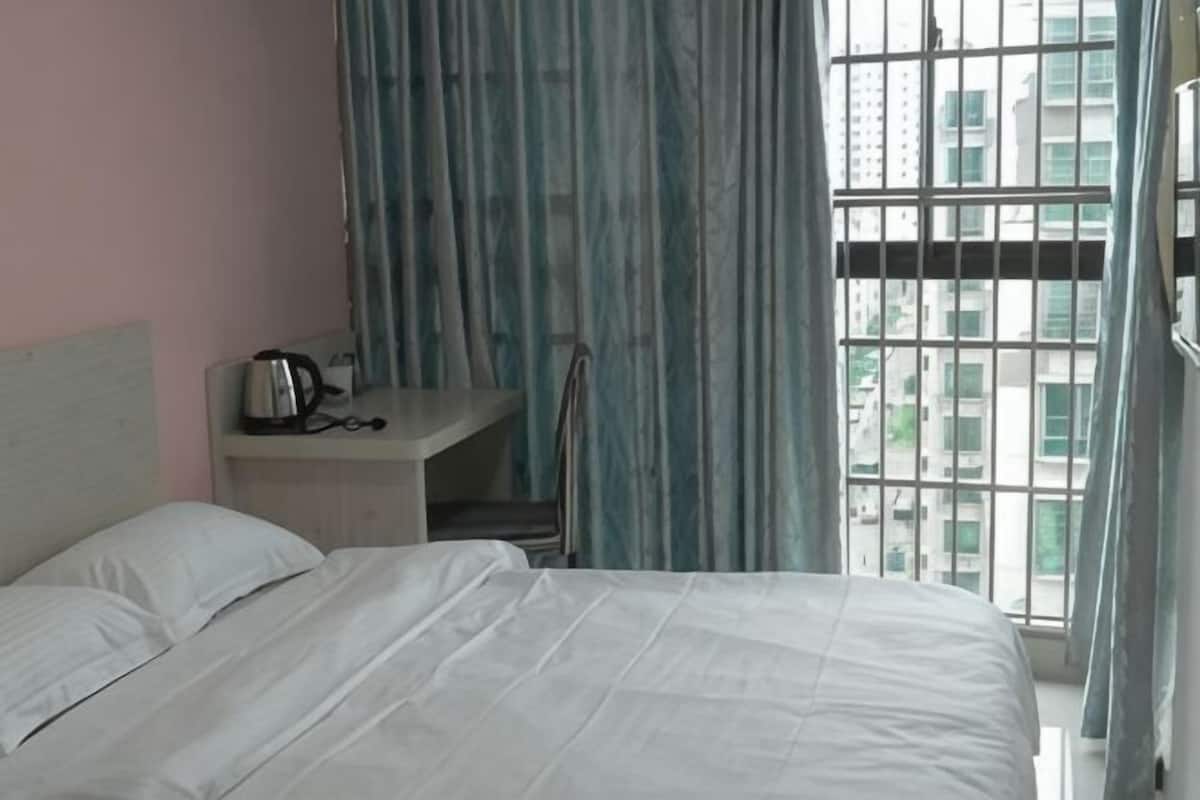 A hotel room with a bed, a desk with a kettle, and a window with curtains.
