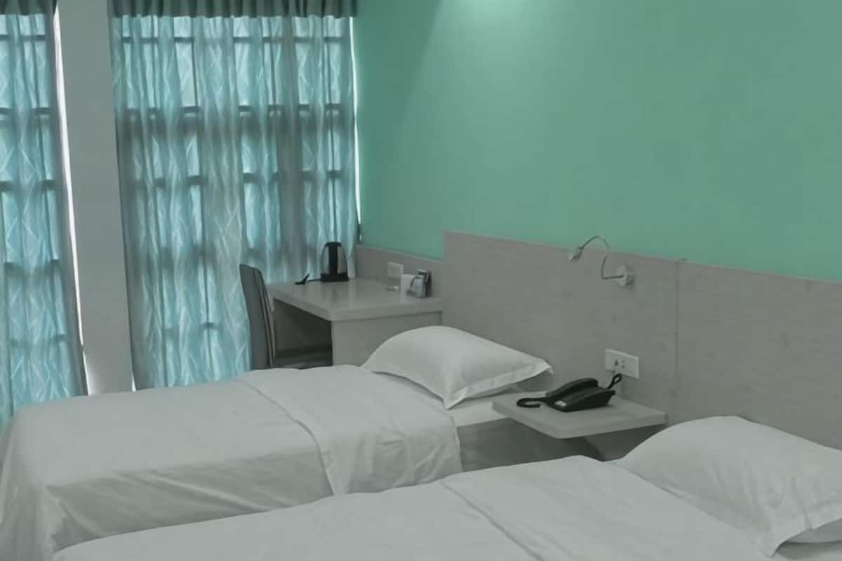A hotel room with two beds, a desk, a telephone, and a window with curtains.