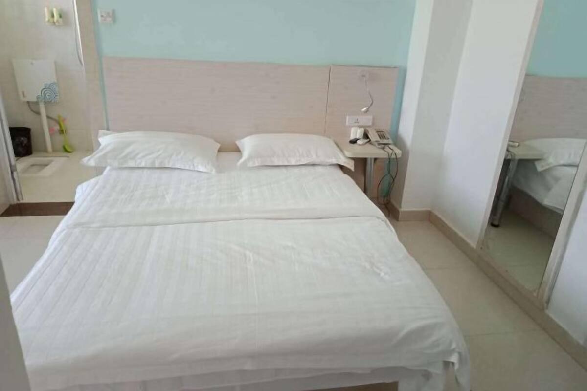 A hotel room with a bed, a bedside table with a lamp, and a mirror.