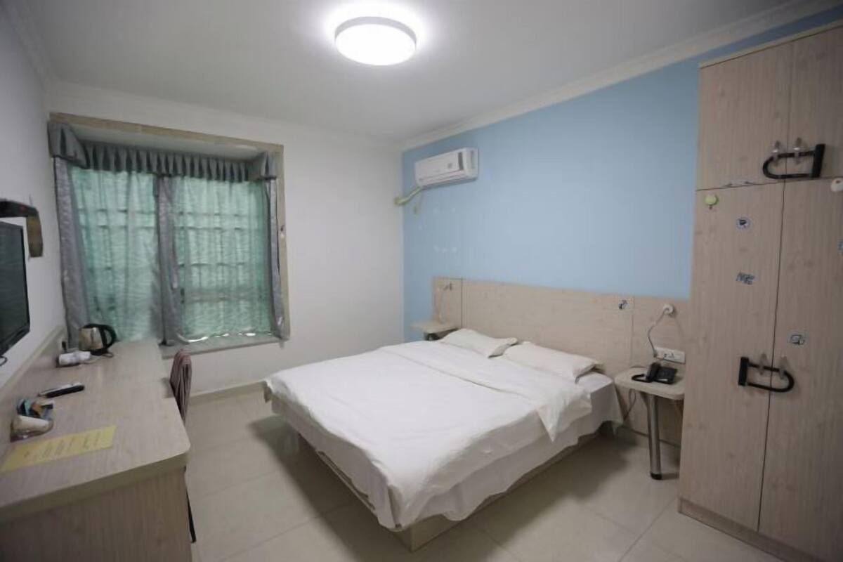 A bedroom with a bed, bedside table, wardrobe, and a window with curtains.