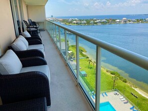 Uma varanda com mobiliário de vime, piscina e vista para a água e edifícios.