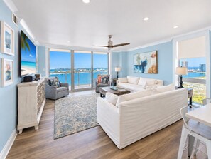 A spacious living room with a large sofa, a dining table, and a view of the ocean through large windows.