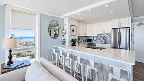 A modern kitchen with white cabinets, a stainless steel refrigerator, and a view of the ocean.