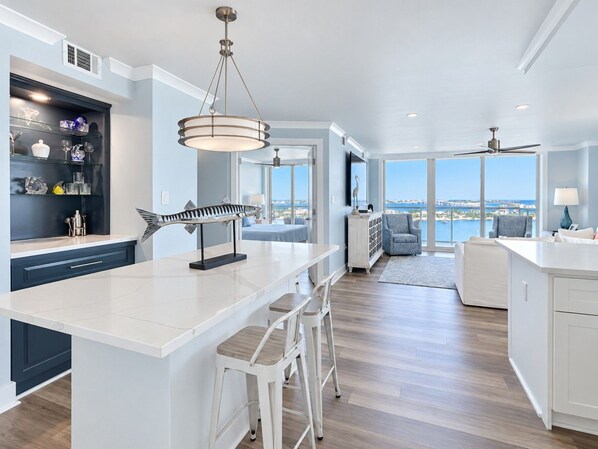 A modern kitchen with a central island, bar stools, and a view of the sea.