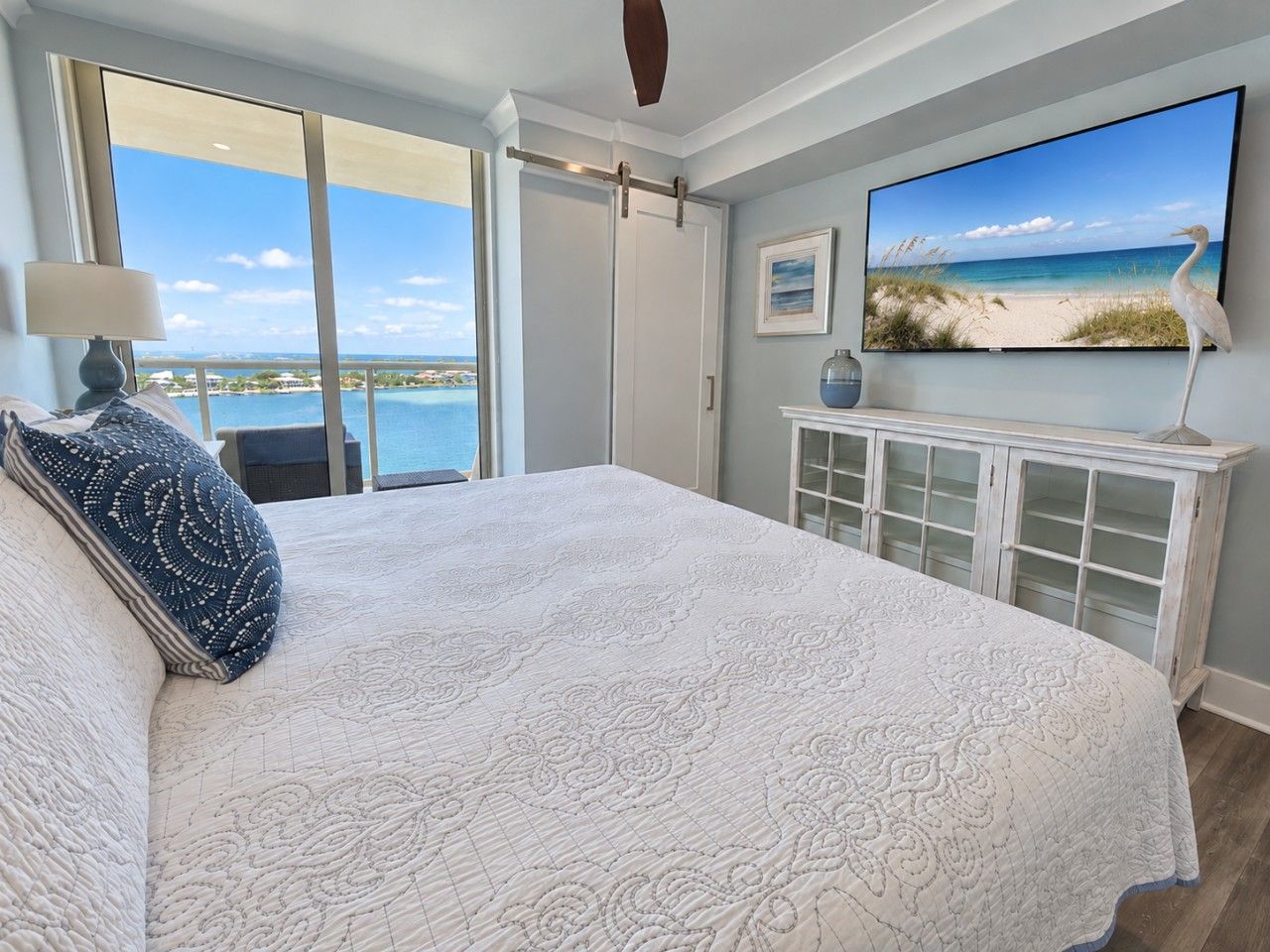 A bedroom with a large bed, a television, a cabinet, and a view of the ocean.