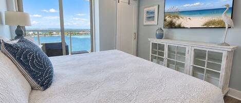 A bedroom with a large bed, a television, a cabinet, and a view of the ocean.