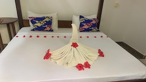 A neatly made bed with a towel arranged in a fan shape, red flowers, and two pillows with a blue and orange pattern.