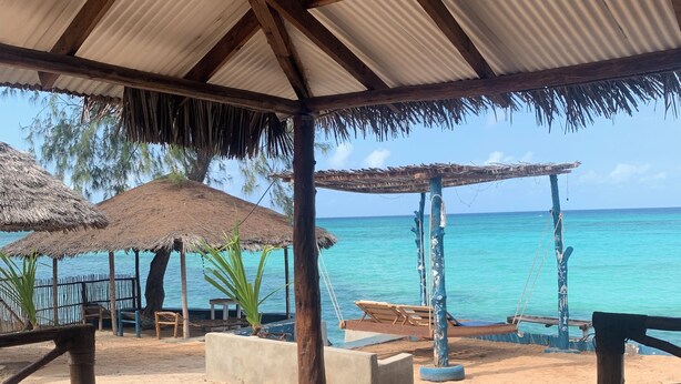A beachside pavilion with a thatched roof, concrete seating, and a view of the turquoise sea.