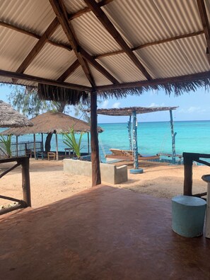 A beachside pavilion with a thatched roof, concrete seating, and a view of the turquoise sea. - Tayana Place (Kizimkazi)