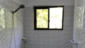 A small, tiled shower room with a window, a showerhead, and a drain.