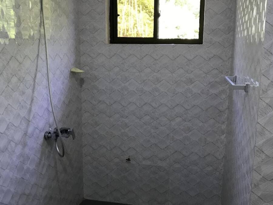 A small, tiled shower room with a window, a showerhead, and a drain.