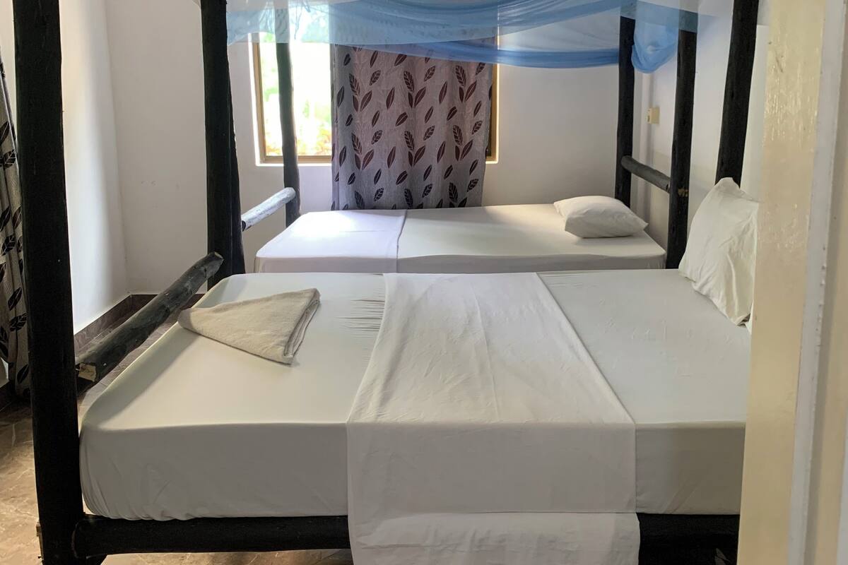 Ein Himmelbett mit Nachttisch und Fenster mit gemusterten Vorhängen.