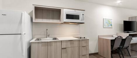 A compact kitchen with a built-in microwave, a refrigerator, and a small dining area with a TV.