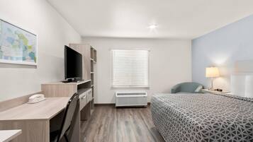 A hotel room with a bed, desk, chair, television, air conditioning unit, and a map on the wall.