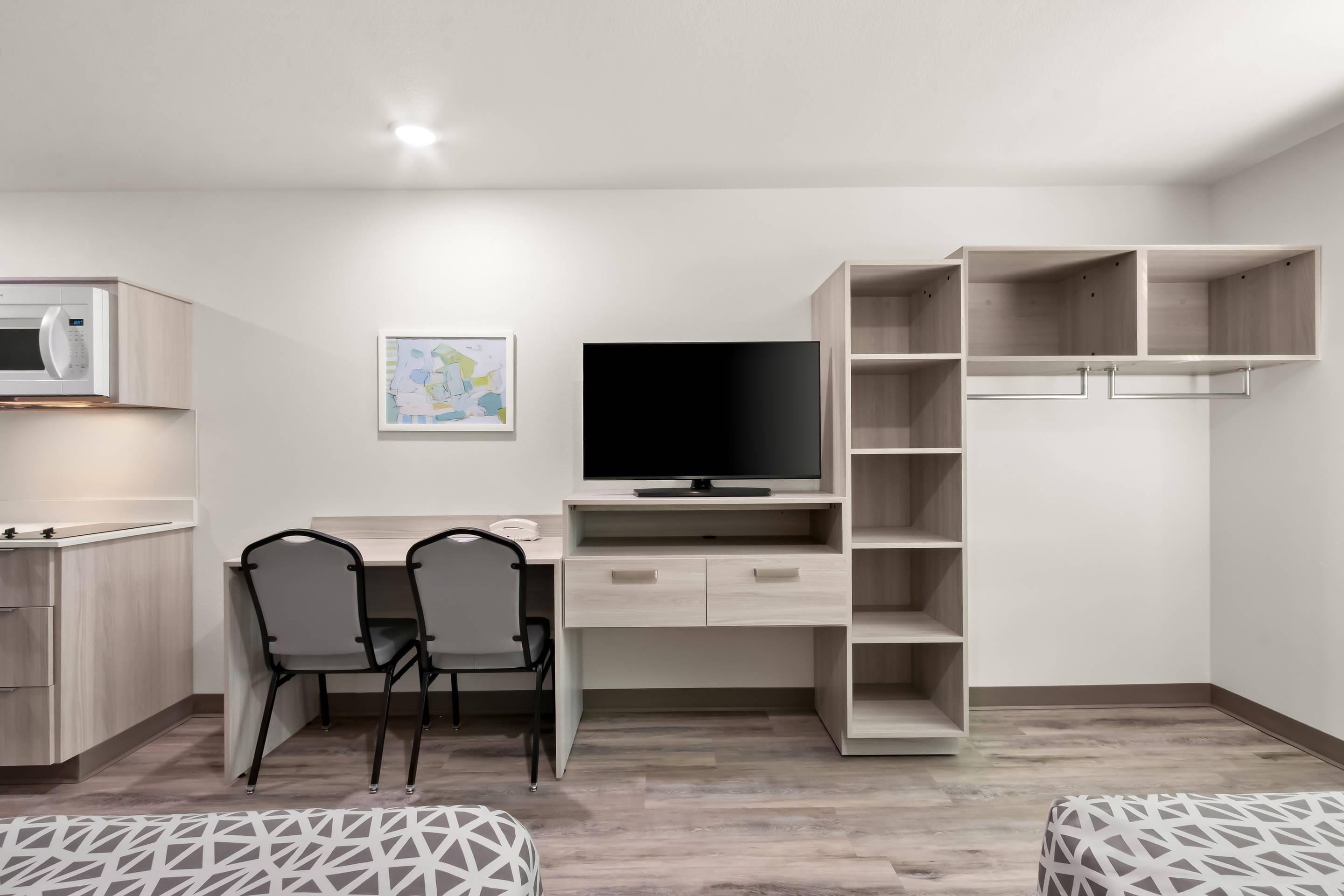 A modern, minimalist room with a desk, two chairs, a flat-screen TV, a microwave, and a wardrobe with open shelves.