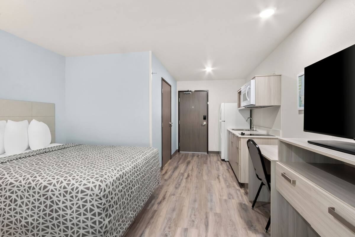 A modern hotel room with a bed, a desk, a chair, a TV, and a door leading to the bathroom.