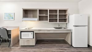 Una cocina moderna con armarios de madera clara, un microondas integrado y un refrigerador blanco.