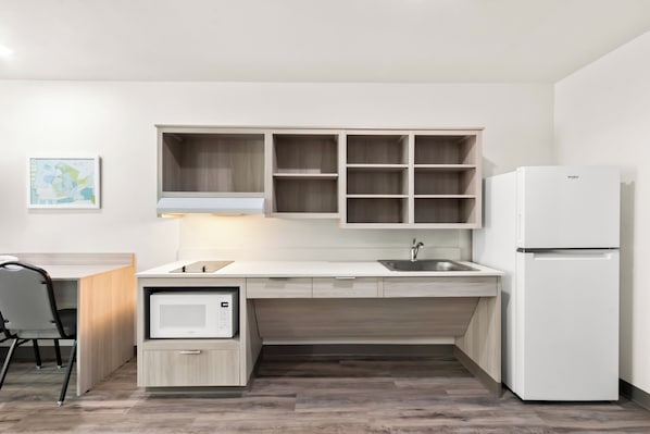 Una cocina moderna con armarios de madera clara, un microondas integrado y un refrigerador blanco.