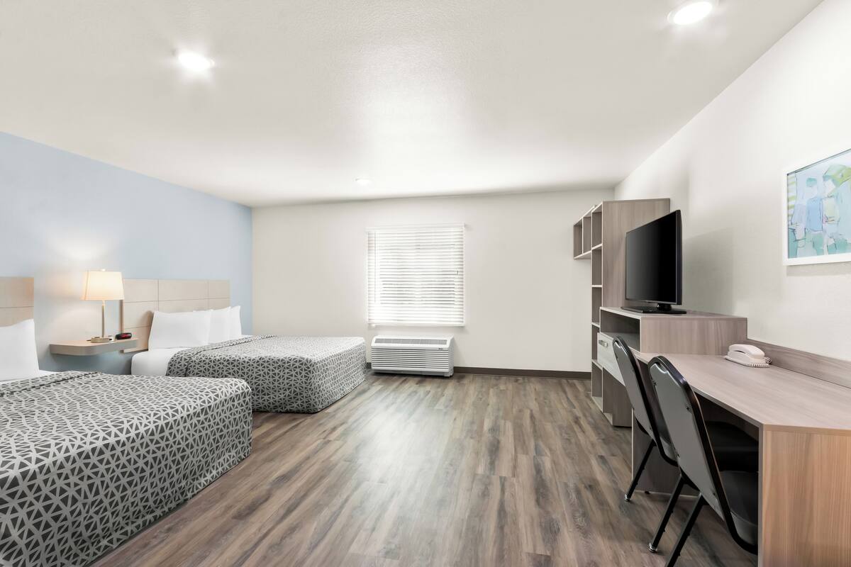 A hotel room with two beds, a desk, a chair, a TV, and a window with blinds.