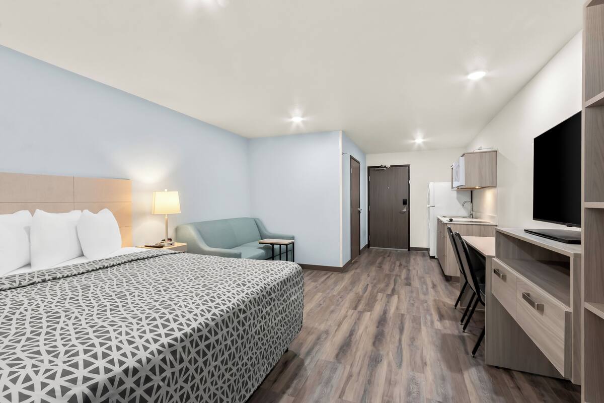 A modern hotel room with a large bed, a desk, a chair, and a TV.