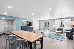 Ein modernes Wohnzimmer mit einem Holzesstisch, grauen Stühlen, einem grauen Sofa und einem blauen Teppich.
