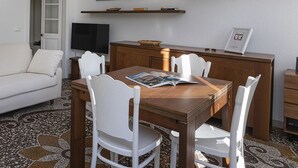 A dining area with a wooden table and white chairs, a television, and artwork on the wall. - La casa di Nanni a Camogli by Wonderful Italy (Camogli)