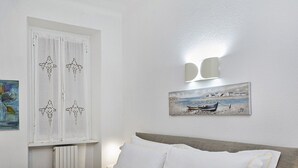 A bedroom with a bed, white curtains, a painting, and a window. - La casa di Nanni a Camogli by Wonderful Italy (Camogli)