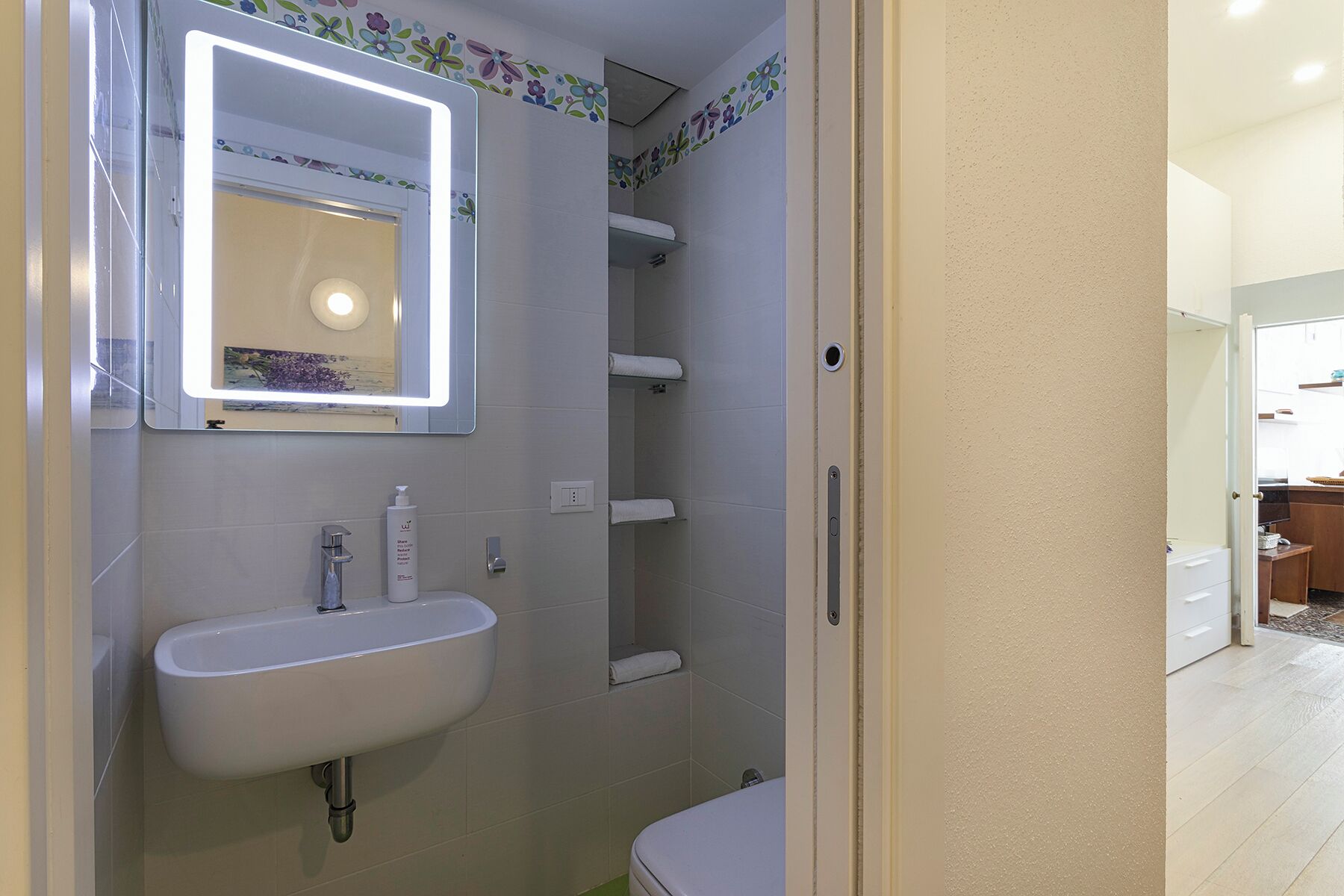 A bathroom with a white sink, a mirror with a light, and a shower area.