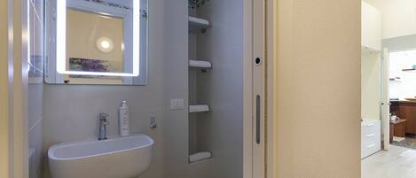 A bathroom with a white sink, a mirror with a light, and a shower area.