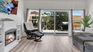 Un salon moderne doté d’une cheminée, d’un fauteuil inclinable, d’un canapé et d’une grande porte-fenêtre coulissante donnant sur une terrasse extérieure.
