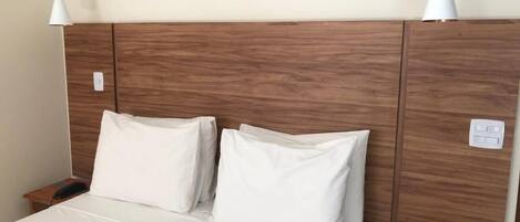A hotel room with a wooden headboard, two white pillows, a white bedspread, and a bedside table with a remote control.