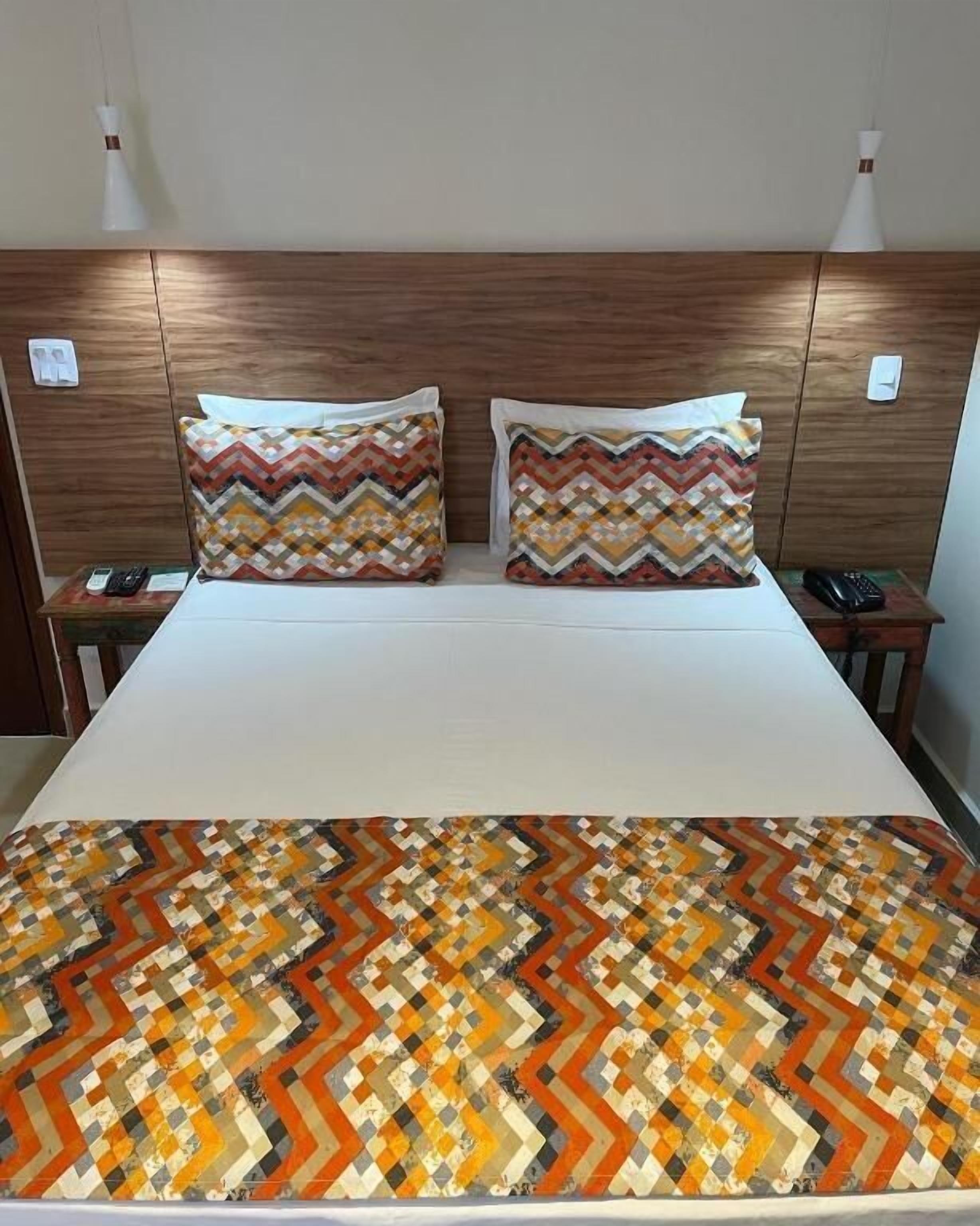 Habitación de hotel con cabecera de madera, dos mesitas de noche con teléfonos y una colcha estampada.