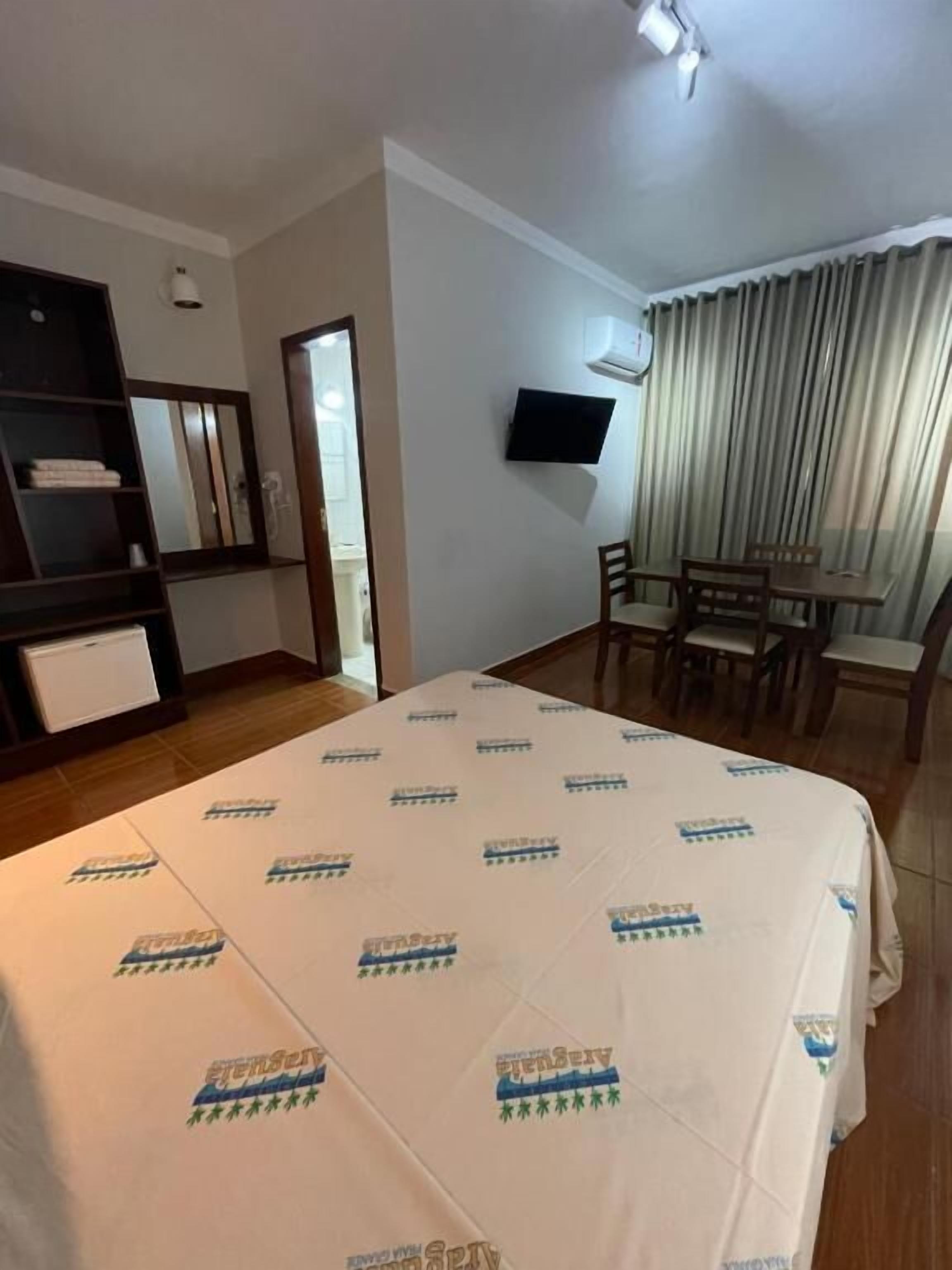 Habitación de hotel con cama, televisor montado en la pared, escritorio con sillas y ventana con cortinas.