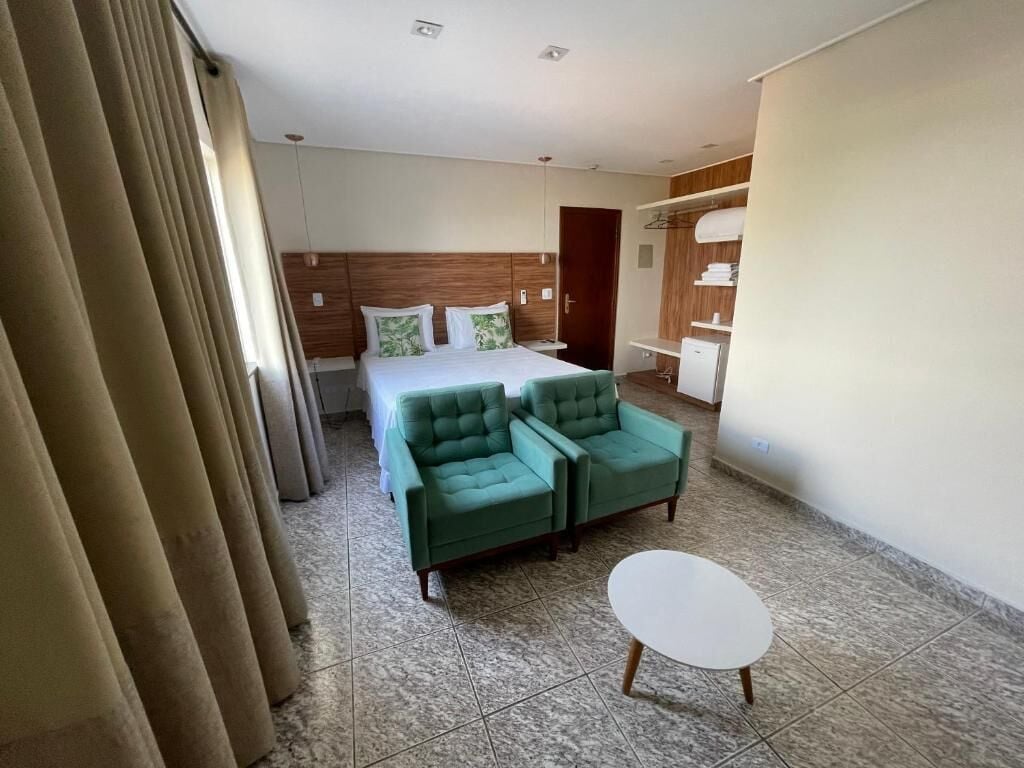 A hotel room with a bed, two green armchairs, a small white table, and a wardrobe.