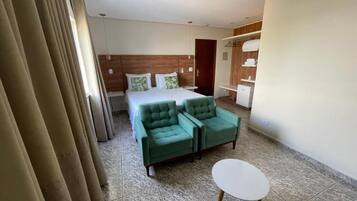 A hotel room with a bed, two green armchairs, a small white table, and a wardrobe.