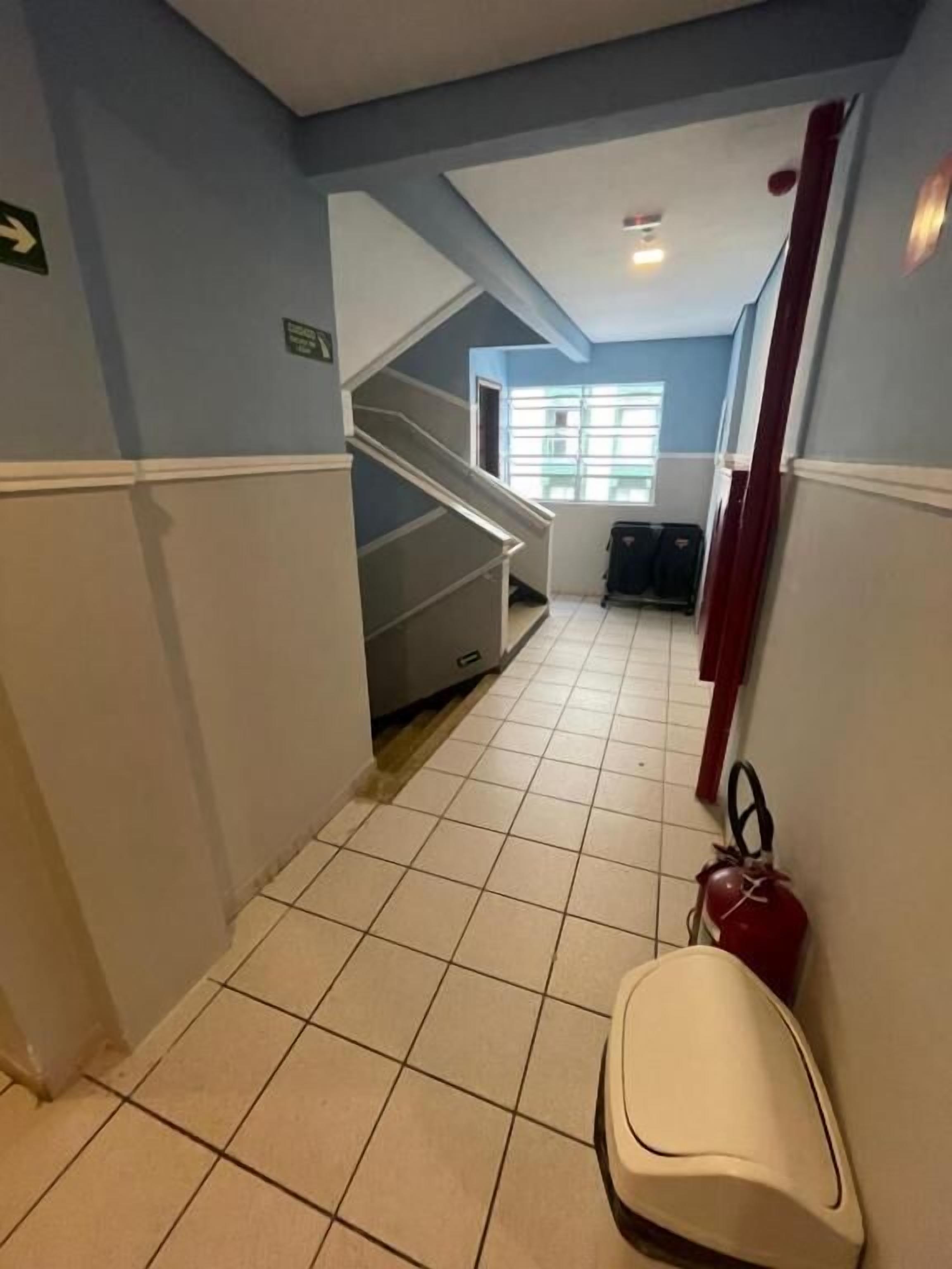 Un pasillo con suelo de baldosas, una escalera, un extintor y una puerta con un letrero.