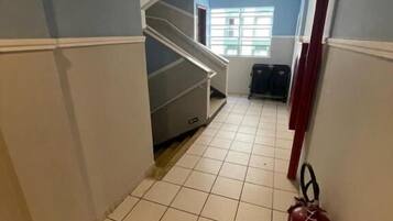 Un pasillo con suelo de baldosas, una escalera, un extintor y una puerta con un letrero.
