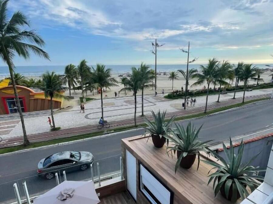 Un balcon donnant sur une plage, des palmiers et une route où circulent des voitures.