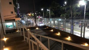 A balcony with a wooden floor and white railings overlooking a street at night. - Hotel Araguaia (Praia Grande)