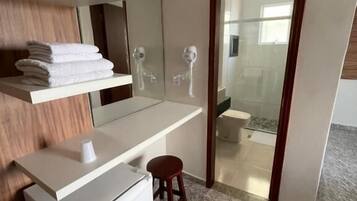 Une salle de bain moderne avec un meuble-lavabo, un miroir, un porte-serviettes, un petit tabouret et un espace douche visible à travers une porte en verre.